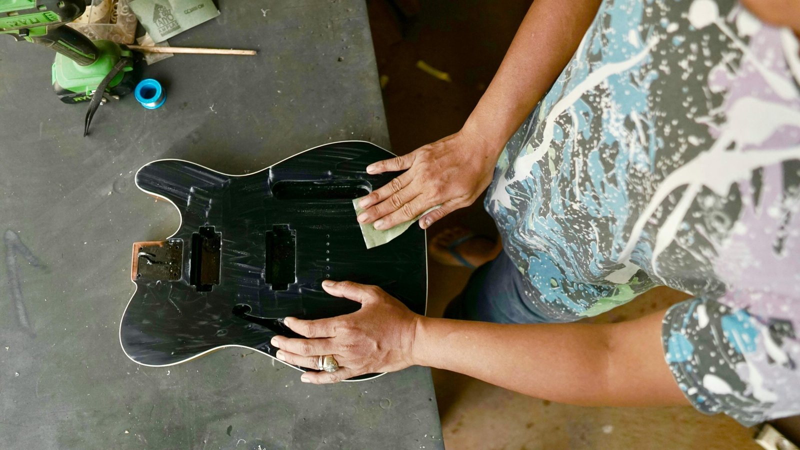 A woman carefully sands a guitar body on a table, highlighting craftsmanship and attention to detail.